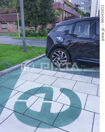 Modern electric car plugged in, charging on the street station. Modern electric car plugged in, charging on the street station. 96045055
