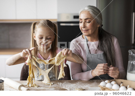 Cheerful caucasian little granddaughter and elderly grandmother make cookie dough, enjoy lesson Cheerful caucasian little granddaughter and elderly grandmother make cookie dough, enjoy lesson 96046622