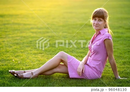 Side view of young cute woman sitting on grass in good weather. Concept of resting on fresh air on nature. 96048130