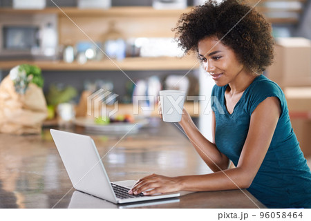 Having coffee with a friend. Young woman using a laptop while drinking from a mug. 96058464