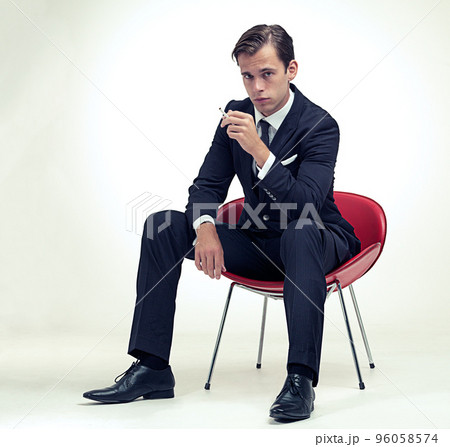 Suave smoker. A studio portrait of a handsome young gentleman in a pinstripe suit sitting on a chair. Suave smoker. A studio portrait of a handsome young gentleman in a pinstripe suit sitting on a chair. 96058574