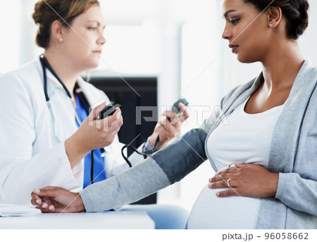Trying to get a reading. Cropped shot of a confident female doctor checking the blood pressure of a pregnant patient at a hospital during the day. 96058662