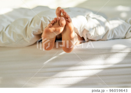 Wiggling toes of wakefulness. Shot of a mans feet poking out from the bottom of his bed. 96059643