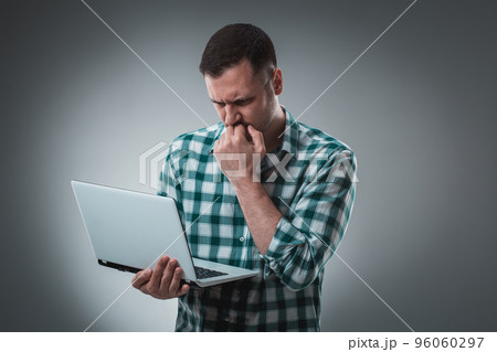Frustrated businessman holding a laptop covers his face with his hand on gray background. 96060297