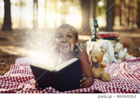 Let reading take you to a magical and wonderful world. Shot of a little girl reading a book with glowing pages in the woods. 96060863