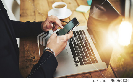 Business with one swipe. Cropped shot of a businessman using a mobile phone and laptop at his work desk. 96060886
