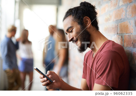 Arranging a date for the weekend. A young man using a mobile phone with his friends standing in the background. 96062335