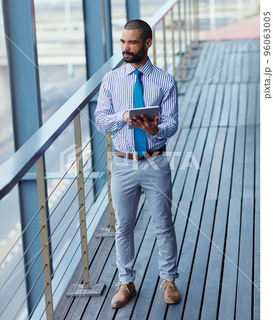 Technology brings business closer to him. Shot of a young businessman using a digital tablet outside of an office building. Technology brings business closer to him. Shot of a young businessman using a digital tablet outside of an office building. 96063005