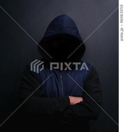 Danger lurks within the dark. Portrait of an unrecognisable hooded man posing against a dark background. Danger lurks within the dark. Portrait of an unrecognisable hooded man posing against a dark background. 96063050