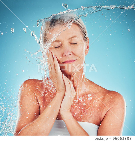 Senior woman, water and skincare for hydrate, hygiene and fresh clean treatment against a blue studio background. Happy elderly female touching face for smooth facial hydration or skin moisture 96063308