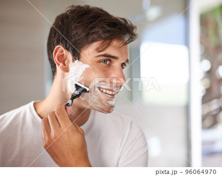 Enjoying his morning routine. Cropped shot of a young man shaving his facial hair with a disposable blade. 96064970
