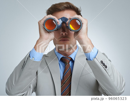 Spying on the competition. A young businessman looking through a pair of binoculars. Spying on the competition. A young businessman looking through a pair of binoculars. 96065323
