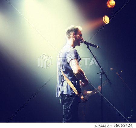 Music from the heart. Shot of a solitary musician playing guitar and singing into a mic. 96065424