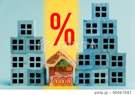 A small origami house made of Russian rubles next to high-rise buildings made of cubes. A bright percentage sign above the money house. The concept of a loan, mortgage and porchase of real estate A small origami house made of Russian rubles next to high-rise buildings made of cubes. A bright percentage sign above the money house. The concept of a loan, mortgage and porchase of real estate 96067682