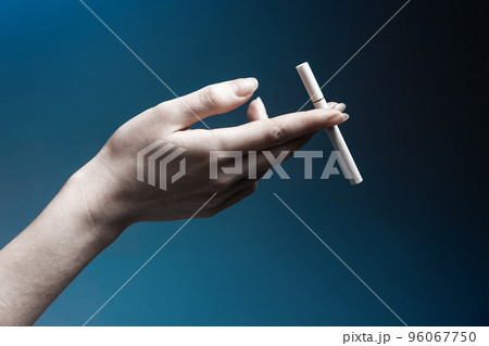 World No Tabacco day. Pale female hand close-up, holding a cigarette gracefully. Dark blue background. The concept of nicotine addiction 96067750