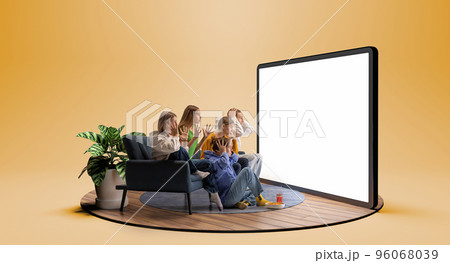 Cheering for favourite team. Young emotional friends watching football match, sport show or movie together. Excited girls and boys sitting in front of huge 3D model of tv screen 96068039