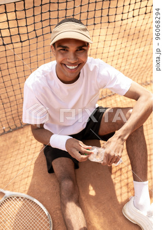 Man in white tshirt and sun visor resting at the tennis courts 96068294