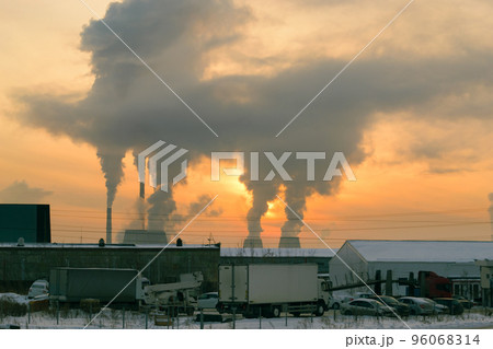 The smoke from the CHP chimneys blocked the sun in the evening sky at sunset. In the foreground is a parking lot with a white truck on it. 96068314