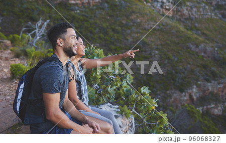 Look at how amazing that view is. Shot of a young couple enjoying the sunset view while out on a hike on a mountain range. 96068327