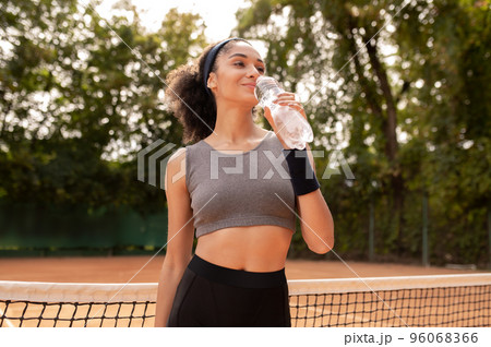 Pretty young girl drinking water after exercising Pretty young girl drinking water after exercising 96068366