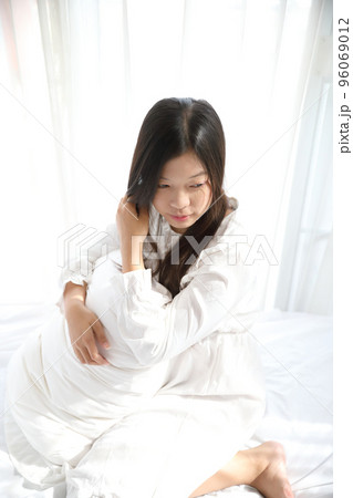 girl sitting with pillow at white bedroom 96069012