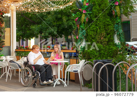 Young daughter and her mother in wheelchair sitting at the table in cafe with drinks and having fun 96072779