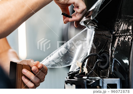 Close up of car wrapping specialist putting protective film on a car in detailing service Close up of car wrapping specialist putting protective film on a car in detailing service 96072878