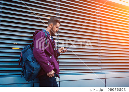 Outdoor fall or winter portrait of handsome hipster man with beard, white t-shirt, blue shirt and maroon jacket holding smartphone Outdoor fall or winter portrait of handsome hipster man with beard, white t-shirt, blue shirt and maroon jacket holding smartphone 96076898