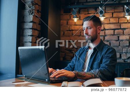 Handsome young man working on laptop while enjoying coffee in cafe 96077072