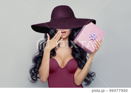 Beautiful Brunette Woman holding pink present gift box wearing wide purple broad brim hat Beautiful Brunette Woman holding pink present gift box wearing wide purple broad brim hat 96077980
