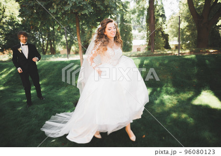 Beautiful romantic wedding couple of newlyweds hugging in park on sunset 96080123