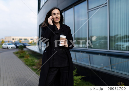 a woman specialist in dealership goes to the office talking on a mobile phone with a glass of coffee a woman specialist in dealership goes to the office talking on a mobile phone with a glass of coffee 96081700