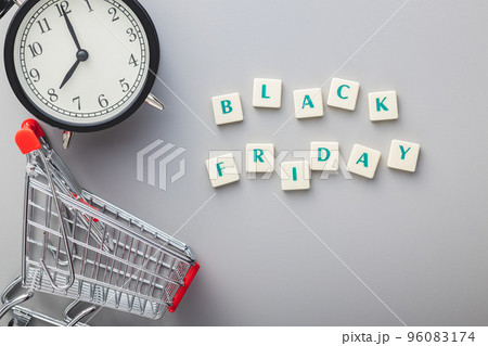 Black friday text, alarm clock and shopping cart on gray background. Top view. Black friday text, alarm clock and shopping cart on gray background. Top view. 96083174