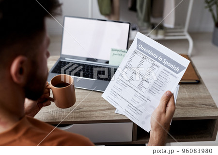 Close-up of young man with cup of tea and paper with questions in Spanish 96083980