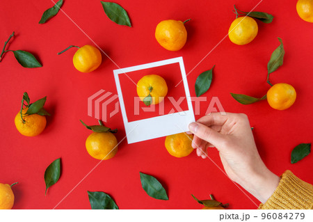 Hand holds white frames with tangerines and green leaves pattern. Xmas creative concept. Flat lay. Christmas layout. Abstract holiday textured backdrop. Creative greeting card design idea 96084279