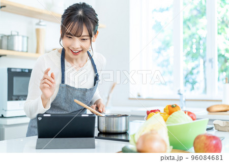 レシピを見ながら料理をするエプロンをした若い女性 レシピを見ながら料理をするエプロンをした若い女性 96084681