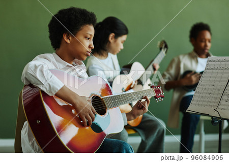 African American schoolgirl with acoustic guitar looking at paper with notes African American schoolgirl with acoustic guitar looking at paper with notes 96084906