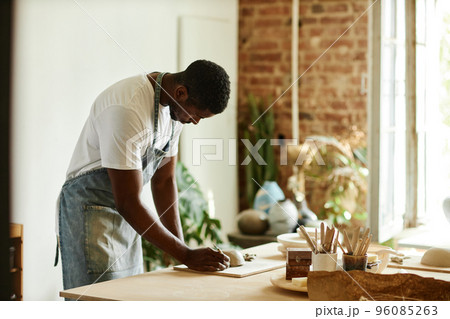 African American man creating beautiful handmade bowl in cozy pottery studio African American man creating beautiful handmade bowl in cozy pottery studio 96085263