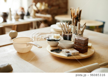 Ceramic cups and art supplies on table in cozy pottery studio Ceramic cups and art supplies on table in cozy pottery studio 96085316