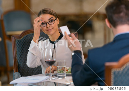 Businessman giving his visit card to woman while having dinner in luxury hotel restaurant Businessman giving his visit card to woman while having dinner in luxury hotel restaurant 96085896