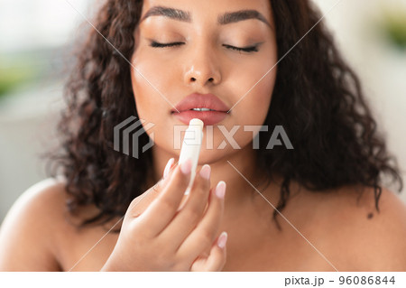 Young african american chubby lady applying lip balm, moisturizing and caring for skin, closeup shot Young african american chubby lady applying lip balm, moisturizing and caring for skin, closeup shot 96086844