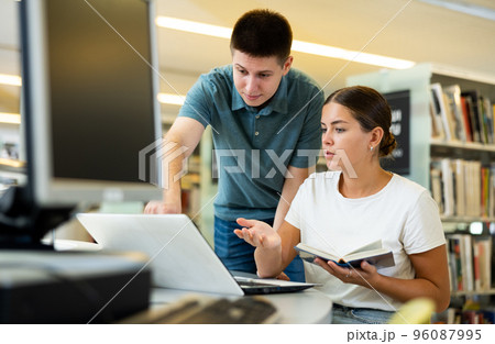 Man in casual clothes asking young lady to be more quiet while she is reading books in the library 96087995
