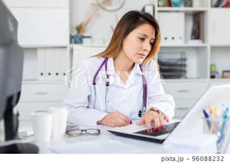 Doctor in uniform is working behind laptop in clinic 96088232