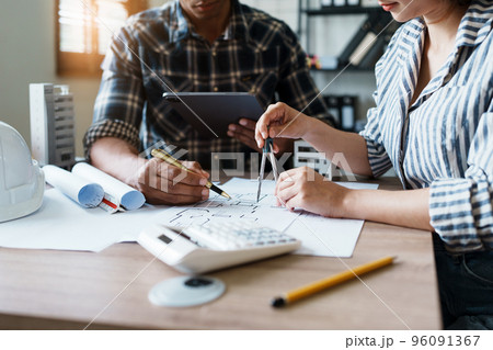 Engineers are consulting the team to design an architectural structure for clients with blueprints and building models to work at office. 96091367