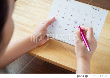 calendar page with female hand holding pen on desk table 96094708