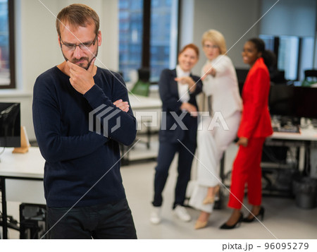 A middle-aged man is upset because of the ridicule of his female colleagues. Discrimination against men in the office. A middle-aged man is upset because of the ridicule of his female colleagues. Discrimination against men in the office. 96095279