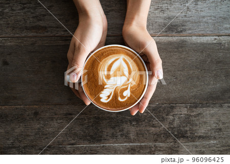 Latte art coffee with swan shape in coffee cup holding by hand 96096425
