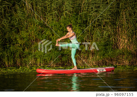 Young woman are doing yoga on a stand up paddle board SUP on a beautiful lake or river 96097155