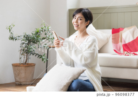 リビングの床に座りスマホを見ている女性 96098377