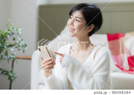 リビングの床に座りスマホを見ている女性 96098384